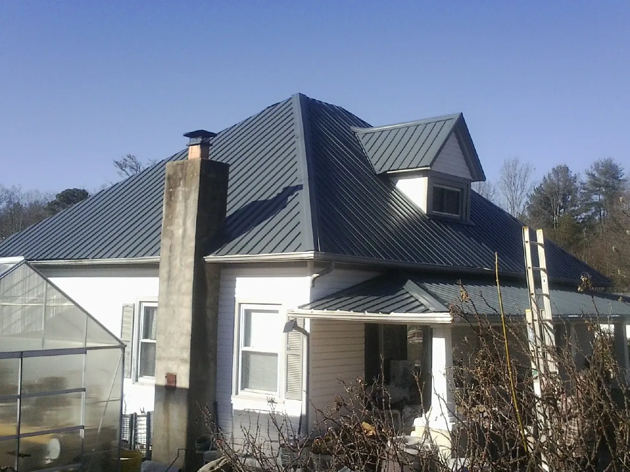 Dark blue standing seam metal roof on a white farmhouse with dormer — Slate & Tile Roof Repair by Roofing Brothers in Polkton