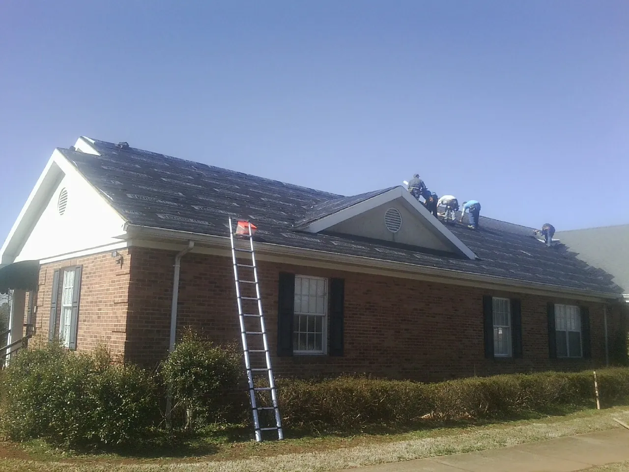 Crew tearing shingles off a brick ranch roof with a ladder set — Emergency Roof Repair work by our crew in Polkton