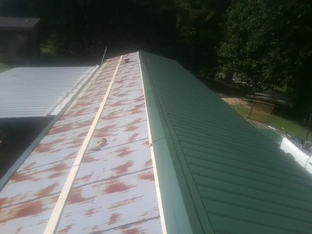Old rusted panels beside newly installed green metal roofing — Wind Damage Roof Repair by Roofing Brothers in Polkton