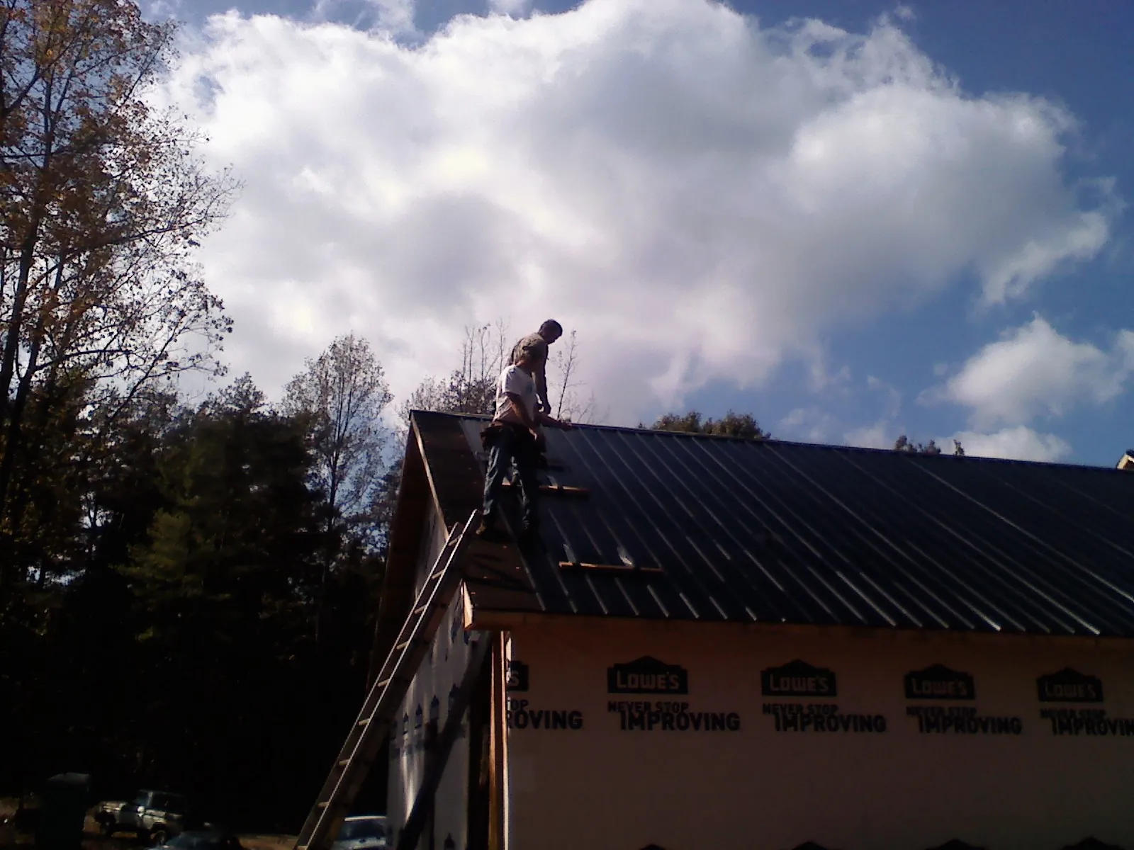 Roofer fastening dark metal panels high against a cloudy sky, from a Roof Inspection job in Polkton