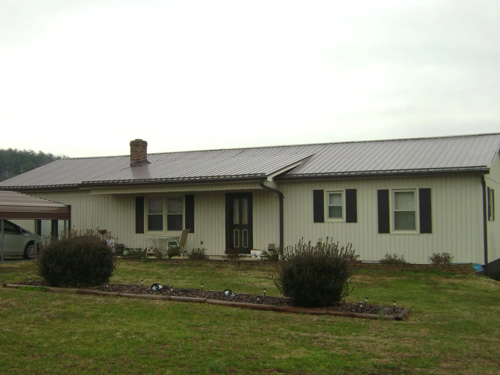Brown metal roof on a cream sided ranch home with a brick chimney in Polkton