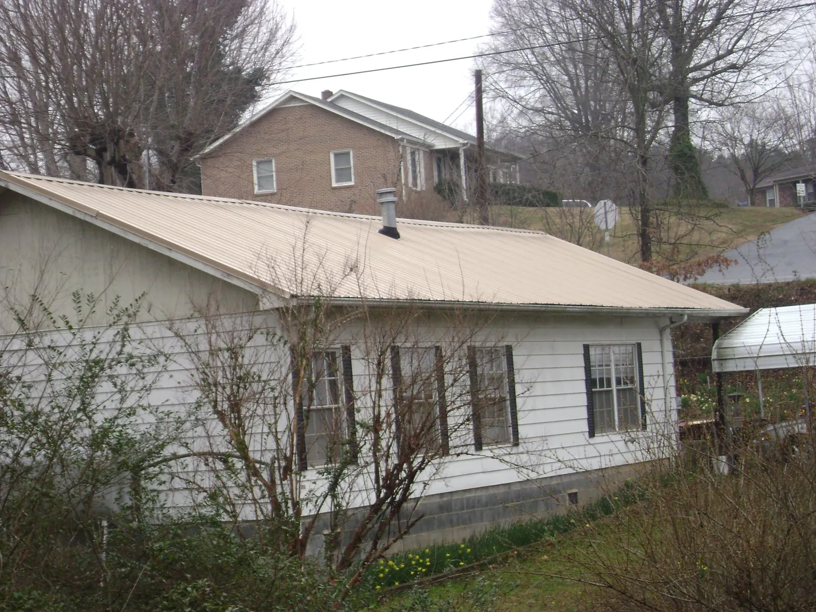 Tan metal roof on a white sided house set into a hillside — Commercial Roofing by Roofing Brothers in Polkton